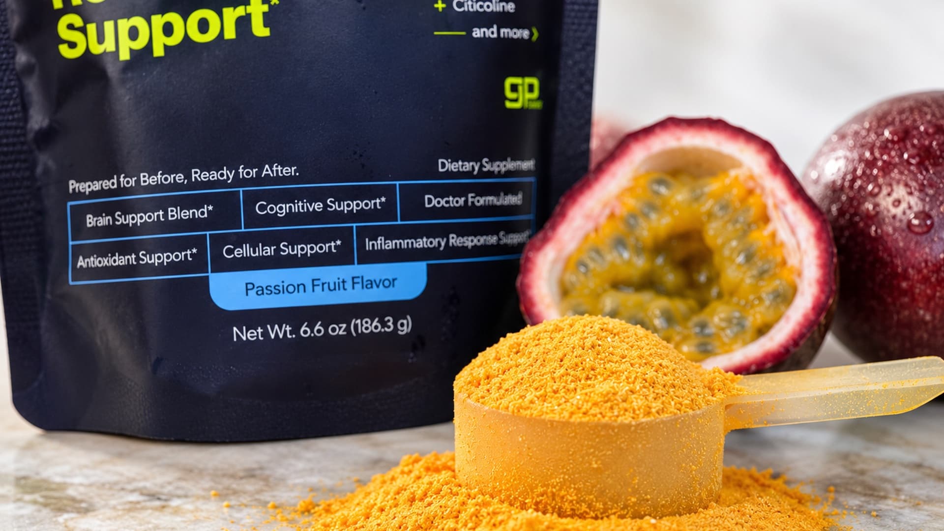 A scoop of passion fruit OnHand powder in front of the pouch, with a cut passion fruit